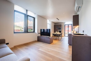 Un soggiorno moderno con una TV a schermo piatto, un'area pranzo con tavolo e sedie, e una cucina con forno e microonde integrati.