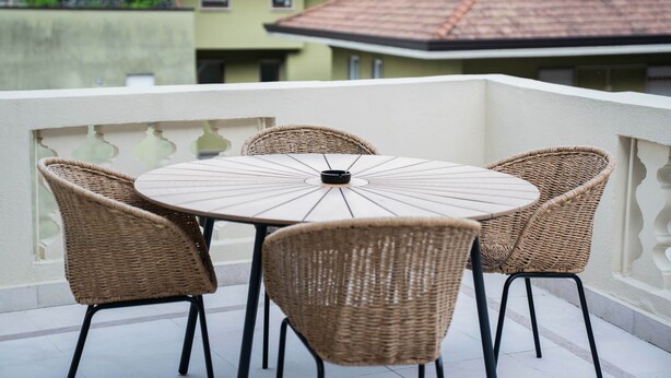 Une table ronde entourée de quatre chaises en osier, sur un balcon doté d’une balustrade blanche.