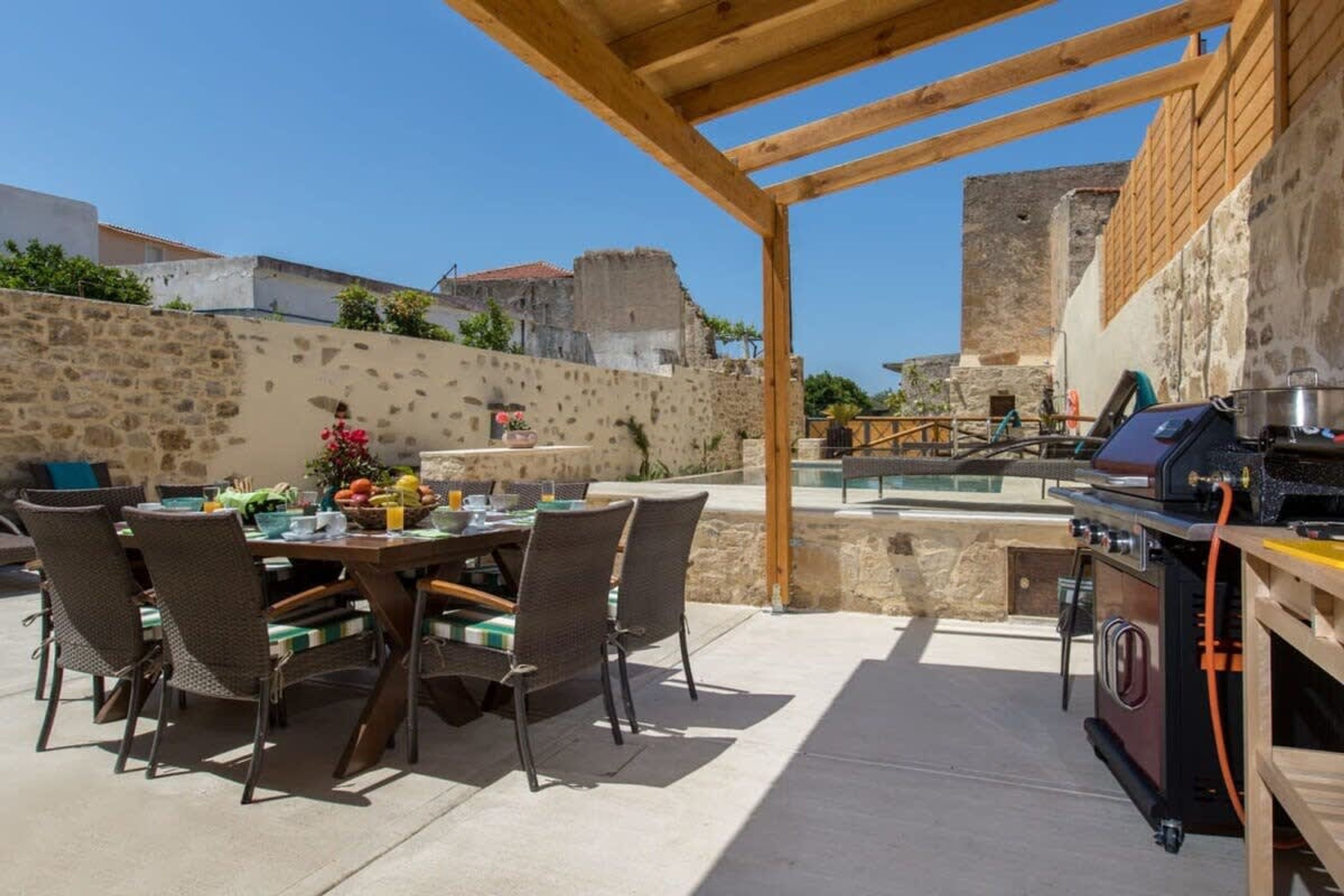 An outdoor patio with a table set for dining, surrounded by stone walls and a view of historic buildings.