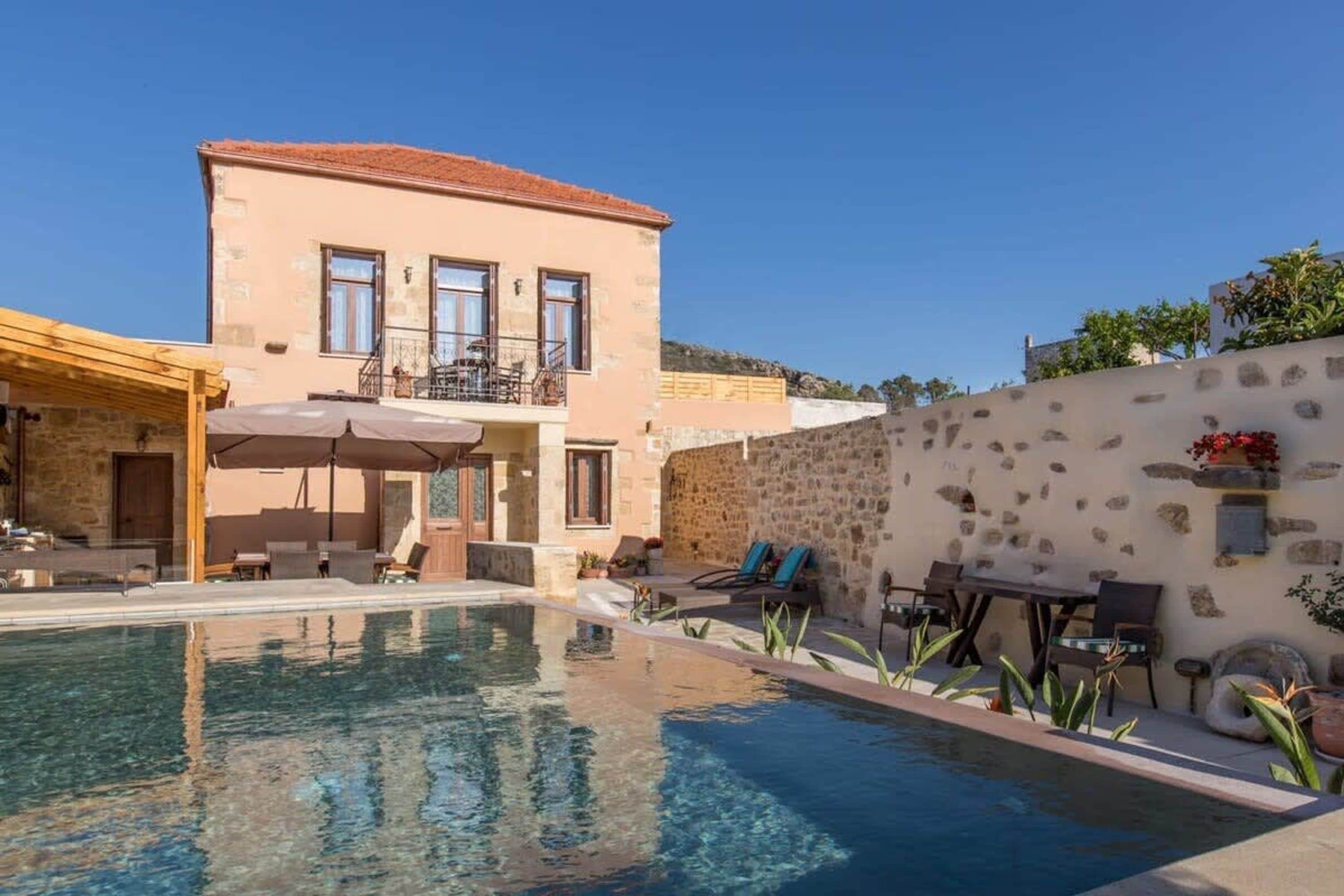 A pool area with a building, outdoor furniture, and a clear sky.