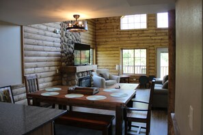 L’intérieur d’une cabane en rondins, avec une table à manger, des chaises, une cheminée et un mur en pierre.