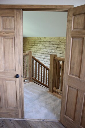 Une porte en bois donnant sur un escalier doté d’une rampe en bois et dont les marches sont recouvertes de moquette.