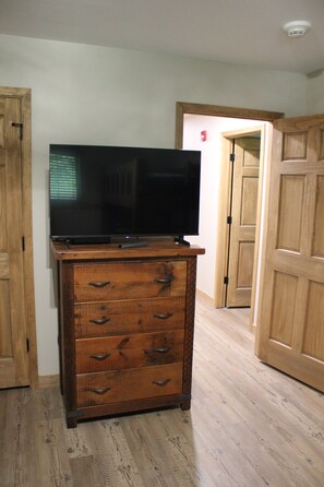 Une commode en bois, dotée de tiroirs, et un téléviseur à écran plat posé sur le dessus, le tout situé dans une pièce dont le sol et les portes sont en bois.