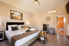 A hotel room with a large bed, a painting, a clock, and a bathroom visible through an open door. - Lamon Villa (Agios Vasileios)