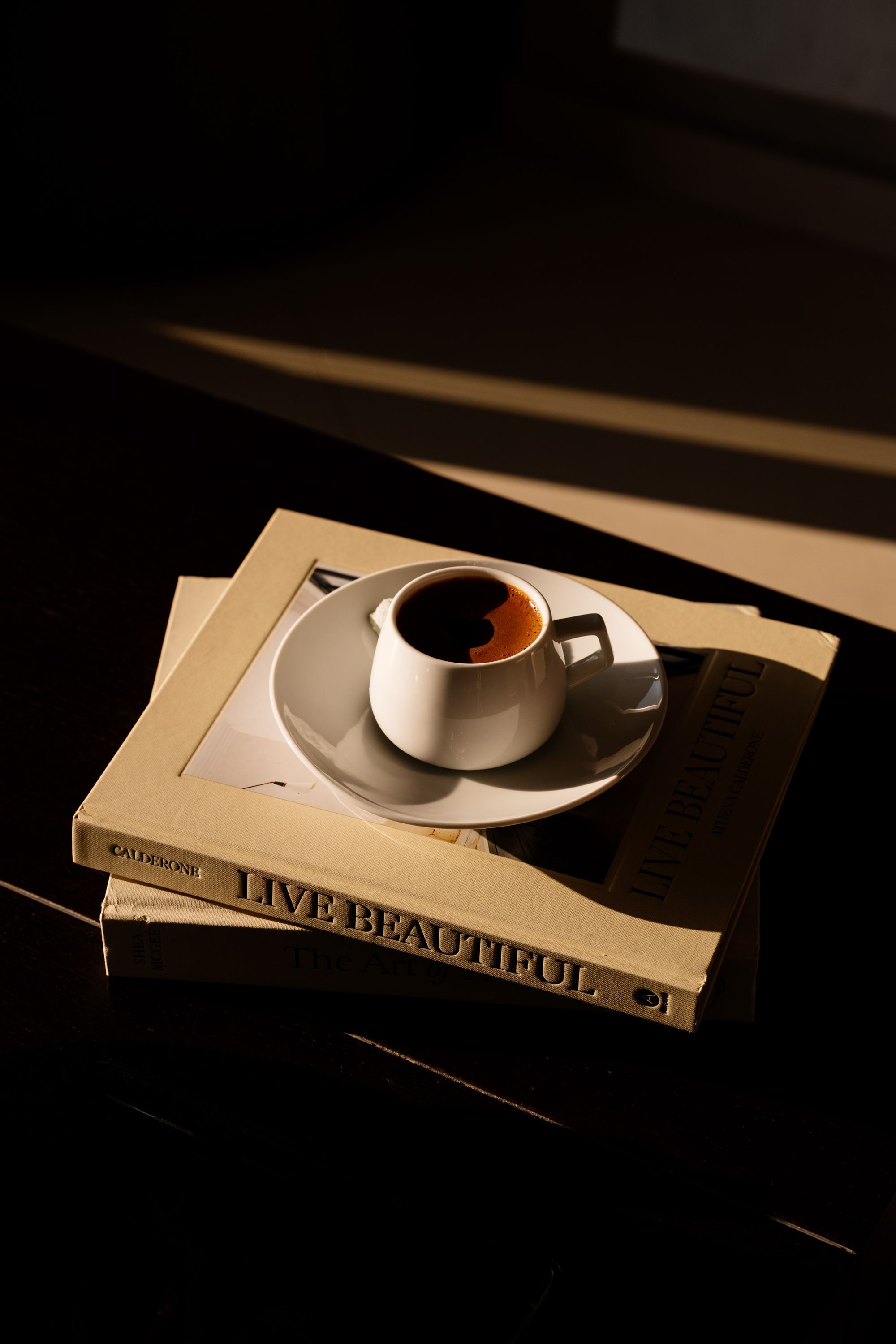 Eine Kaffeetasse auf einer Untertasse, platziert auf einem Buch mit dem Titel 'LIVE BEAUTIFUL', wobei eine Seitenummer sichtbar ist.