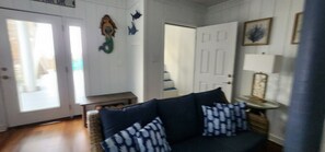Ein Zimmer mit einem dunkelbraunen Sofa, das mit gemusterten Kissen ausgestattet ist, einer hölzernen Bank, einer Tür mit weißem Rahmen und einer Wand mit einem gerahmten Bild.