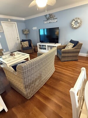 A living room with wicker furniture, a flat-screen TV, and a decorative wall sign. - 5BR On Beach $700+ in freebies and activities (Miramar Beach)
