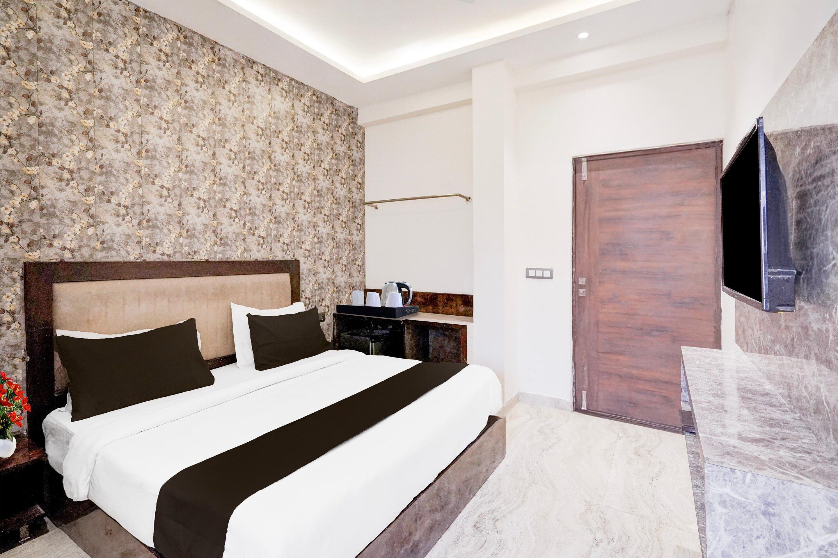 A modern hotel room with a large bed, a flat-screen TV mounted on the wall, and a wooden door.