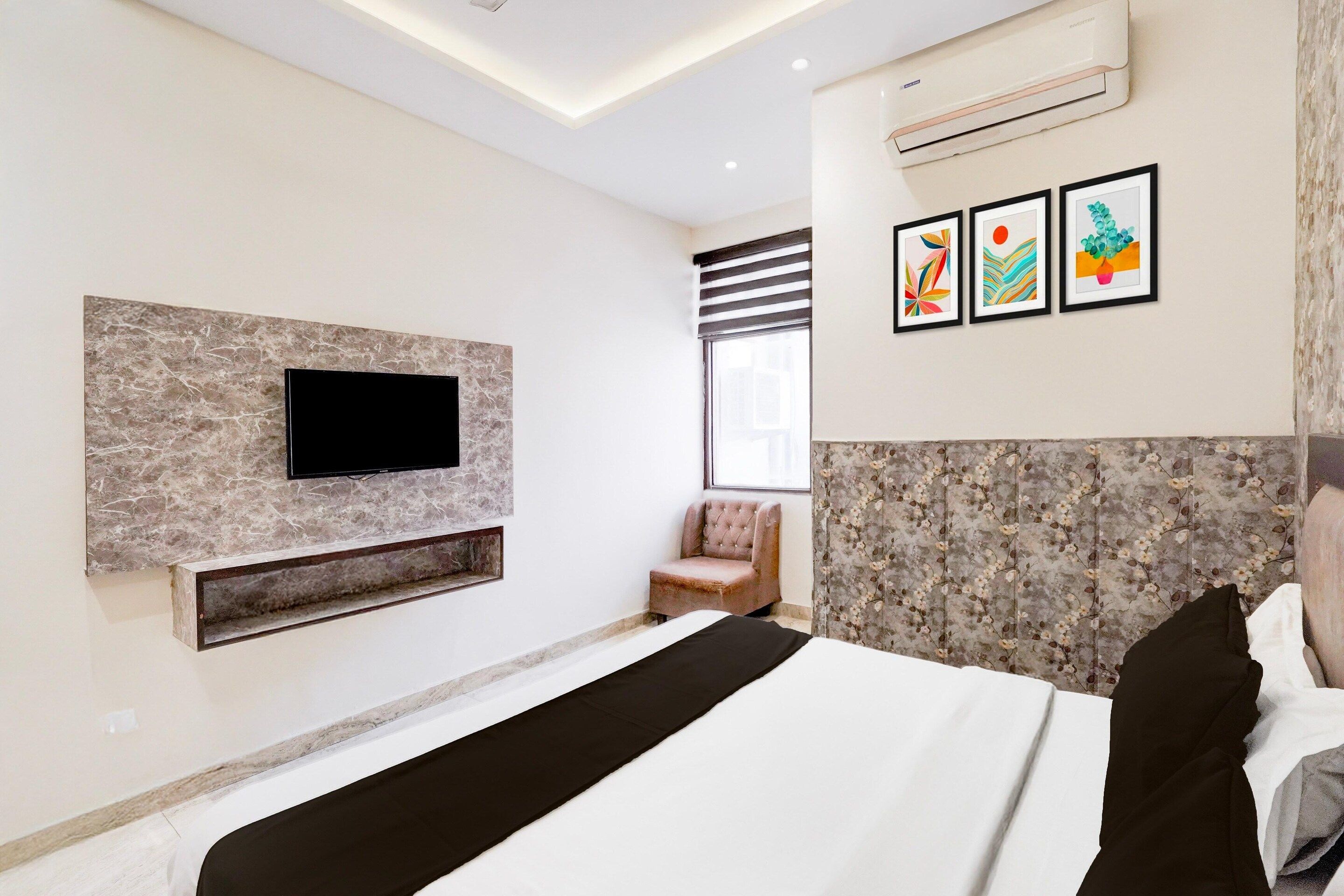 A modern bedroom with a flat-screen TV mounted on a marble wall, a bed with a black and white bedspread, and a chair.