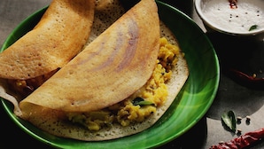 A plate with two folded crepes, a bowl of yellow curry, and a small bowl of white sauce. - Premium A&V Residency (Noida)