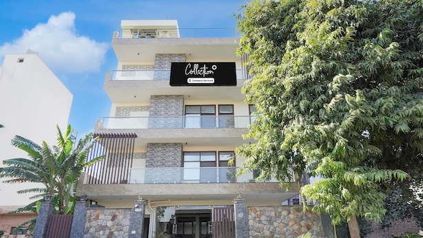 A multi-story building with a signboard, stone facade, and a large tree in the foreground. - Premium A&V Residency (Noida)