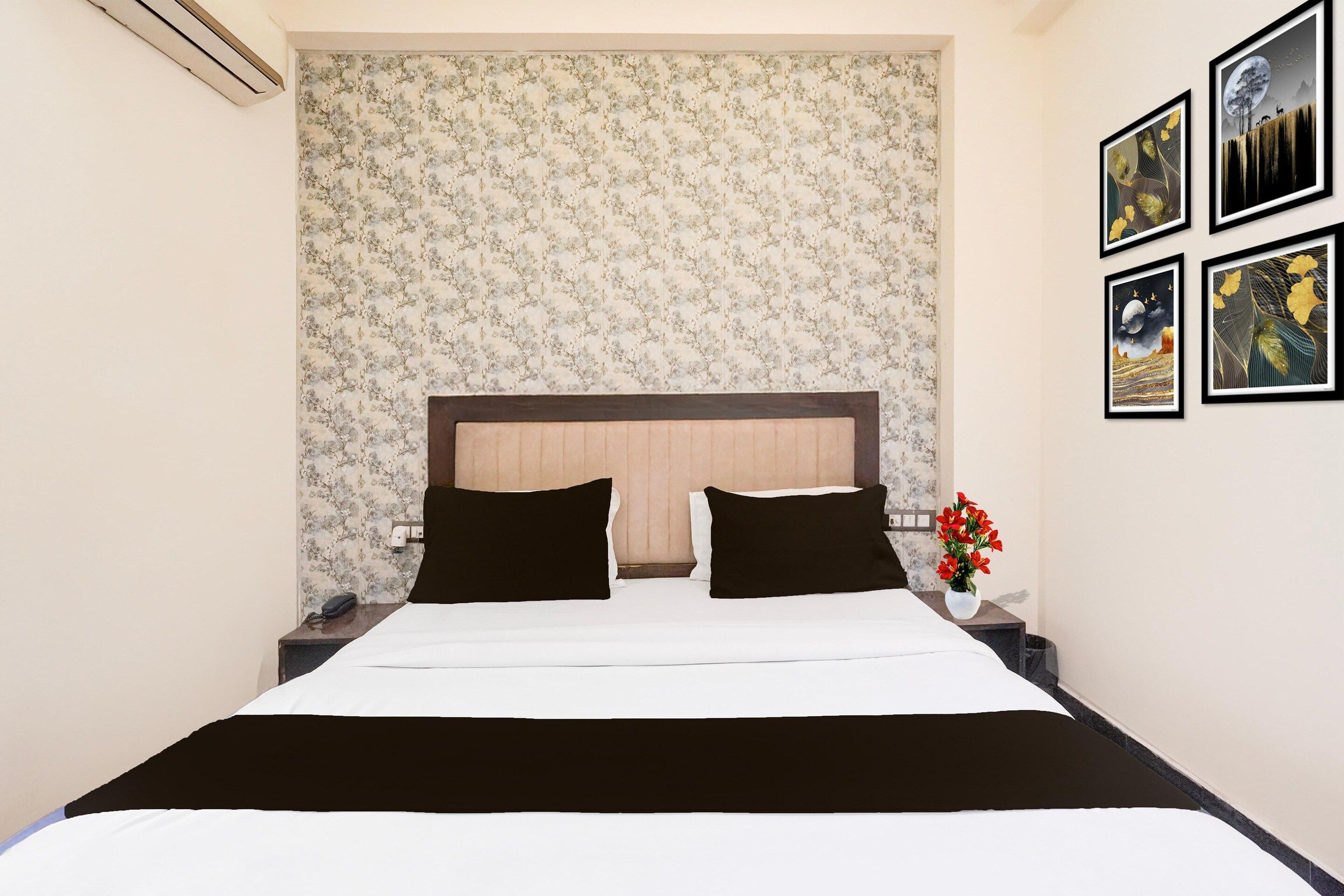 A hotel room with a bed, a nightstand, a vase with flowers, and framed pictures on the wall.