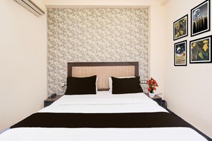 Una habitación de hotel con una cama, una mesita de noche, un jarrón con flores y cuadros en la pared.
