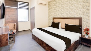 A hotel room with a bed, a chair, a desk, a window, and a wall with floral wallpaper. - Premium A&V Residency (Noida)