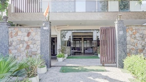 A gated entrance to a building with a stone facade, a small lawn area, and potted plants. - Premium A&V Residency (Noida)