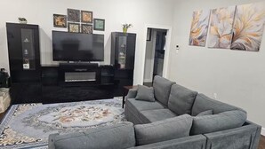 A living room with a grey sectional sofa, a flat-screen TV, a decorative rug, and a black entertainment unit with framed artwork. - Executive Spacious 4-bedroom house in charming Abilene neighborhood. (Abilene)