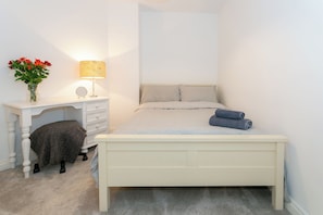 A bedroom with a bed, a bedside table with a lamp, a chair, and a small table with a vase of flowers. - Cosy King's Road Flat - with off-road Parking (Harrogate)