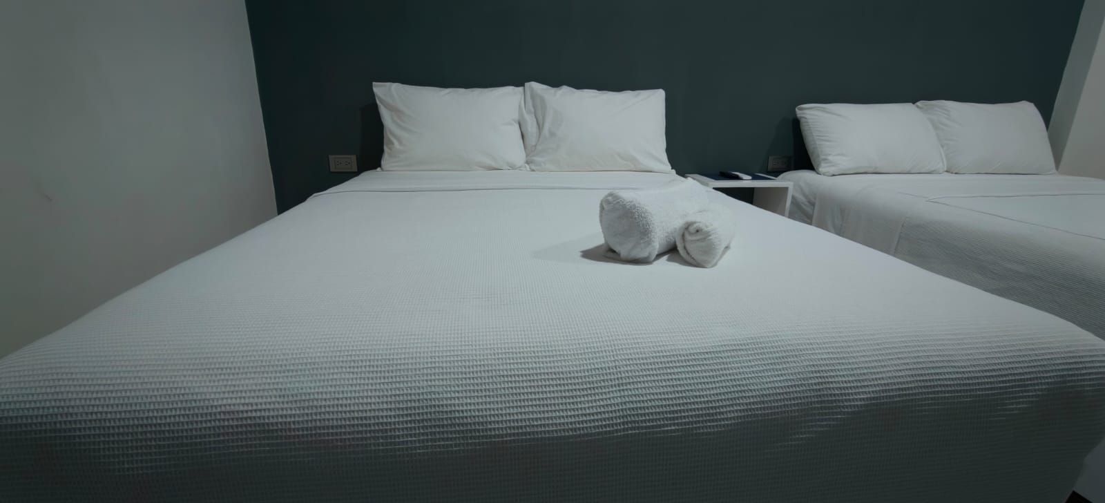 Quarto de hotel com duas camas, cada uma com roupa de cama e almofadas brancas, e um par de toalhas na cama em primeiro plano.