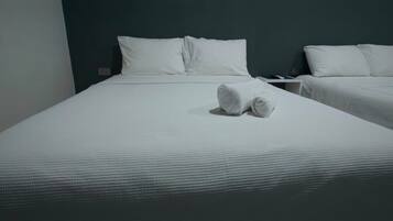 Quarto de hotel com duas camas, cada uma com roupa de cama e almofadas brancas, e um par de toalhas na cama em primeiro plano.
