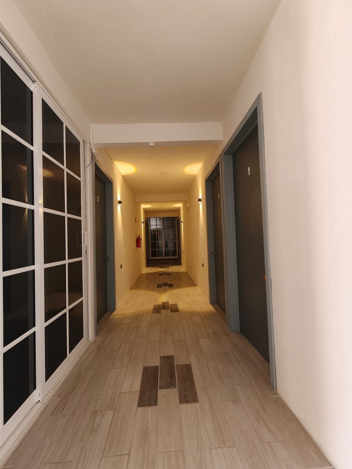 Um corredor com piso de azulejos, um extintor de incêndio e uma porta numerada.