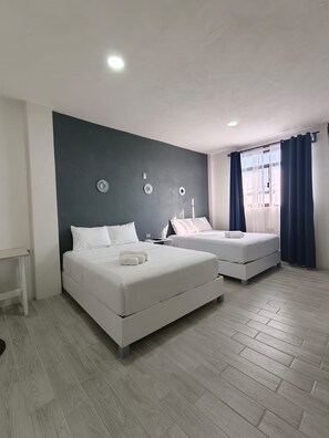 A bedroom with two beds, a small table, and a window with curtains.