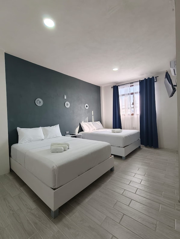 A hotel room with two beds, a dark accent wall, a window with curtains, and a ceiling light.