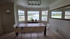 A dining room with a large table and chairs, large windows with a view of the outdoors, and a decorative mirror on the wall. - Luxury Glamping Estate with Hot Tub Near San Jose (Gilroy)