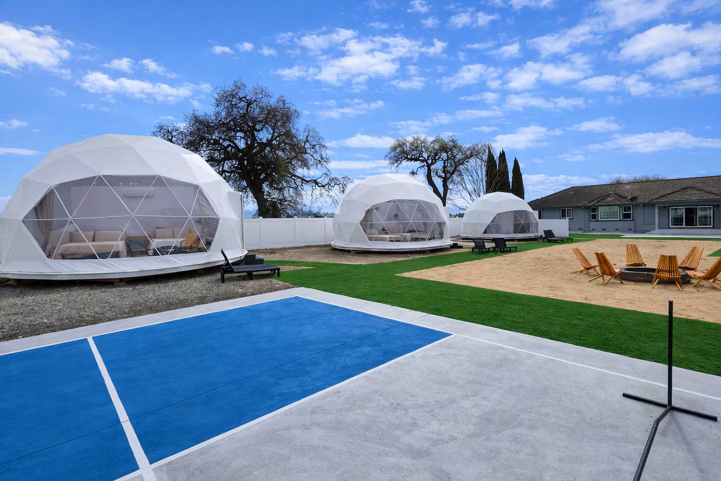 Three dome-shaped yurts with a pool and lounge chairs in a backyard.