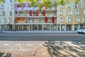 Un edifici de diversos pisos amb entrada a nivell del sòl, balcons amb baranes de vidre i una botiga amb senyalització.