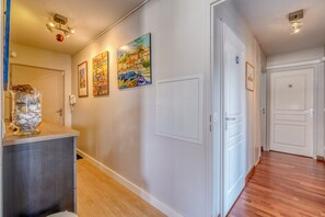 A hallway with wooden flooring, white walls, and a door with a small picture. There are three framed artworks on the wall. - Stunning Flat • AC & Parking in Bordeaux (Bordeaux)