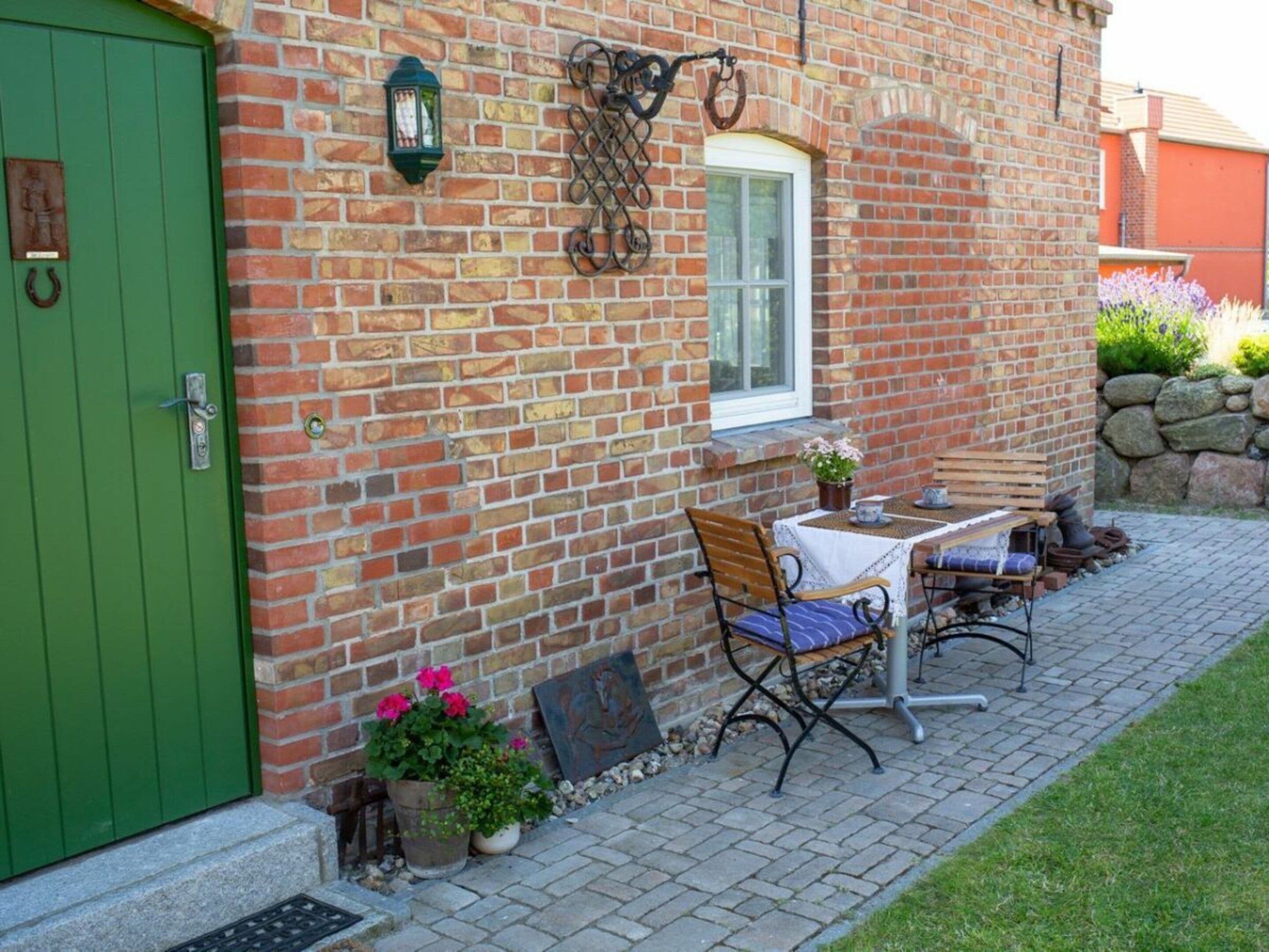 A brick building with a green door, a window, and a patio area with a table and chairs.