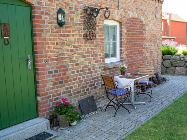A brick building with a green door, a window, and a patio area with a table and chairs.