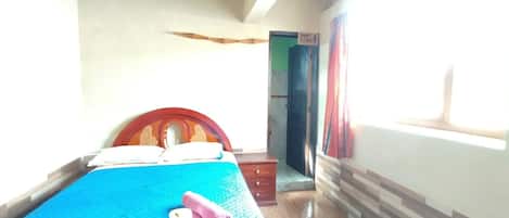 A room with a bed, a wooden headboard, a blue bedspread, a wooden floor, a door, and a window.
