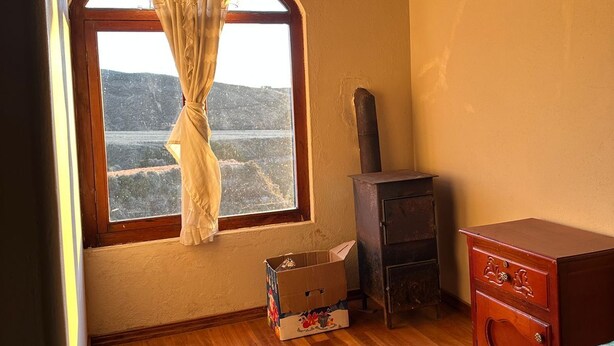 A room with a wooden floor, a window with curtains, a small wooden cabinet, and a box on the floor.