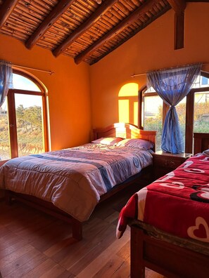 Un dormitorio con dos camas, vigas de madera en el techo y ventanas grandes con cortinas.