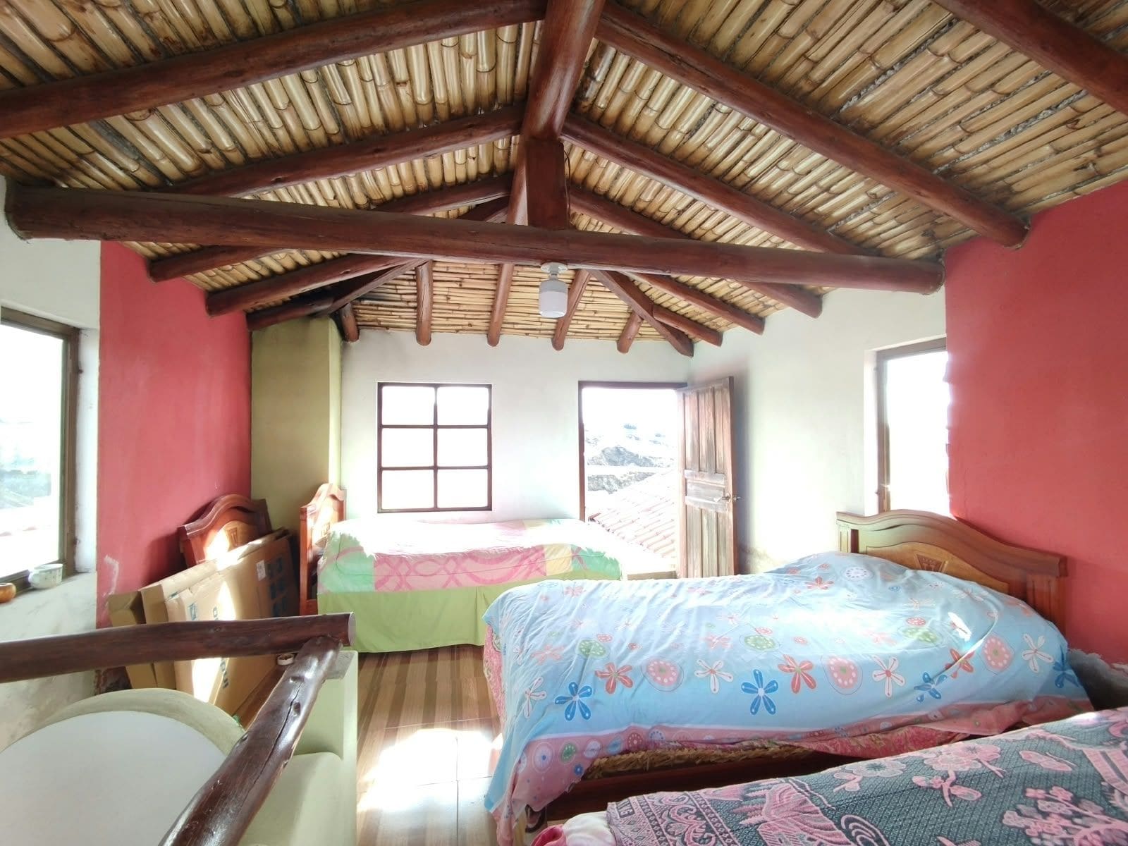 A room with a bamboo roof, a bed with floral bedding, a window, and a door.