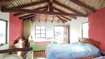 A room with a bamboo roof, a bed with floral bedding, a window, and a door.