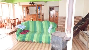 Ein Zimmer mit einem grün gestreiften Sofa, Holzmöbeln, einer Treppe und einem Fliesenboden.