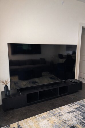 A flat-screen TV mounted on a black stand with a remote control on top. - Vibrant DT Condo NR Farmers Market (Dallas)