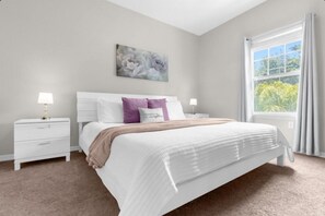 A bedroom with a bed, nightstands, a window with curtains, and a wall-mounted painting. - 8 guests /4 beds /3 baths /Lucaya Village (13-108) (Kissimmee)