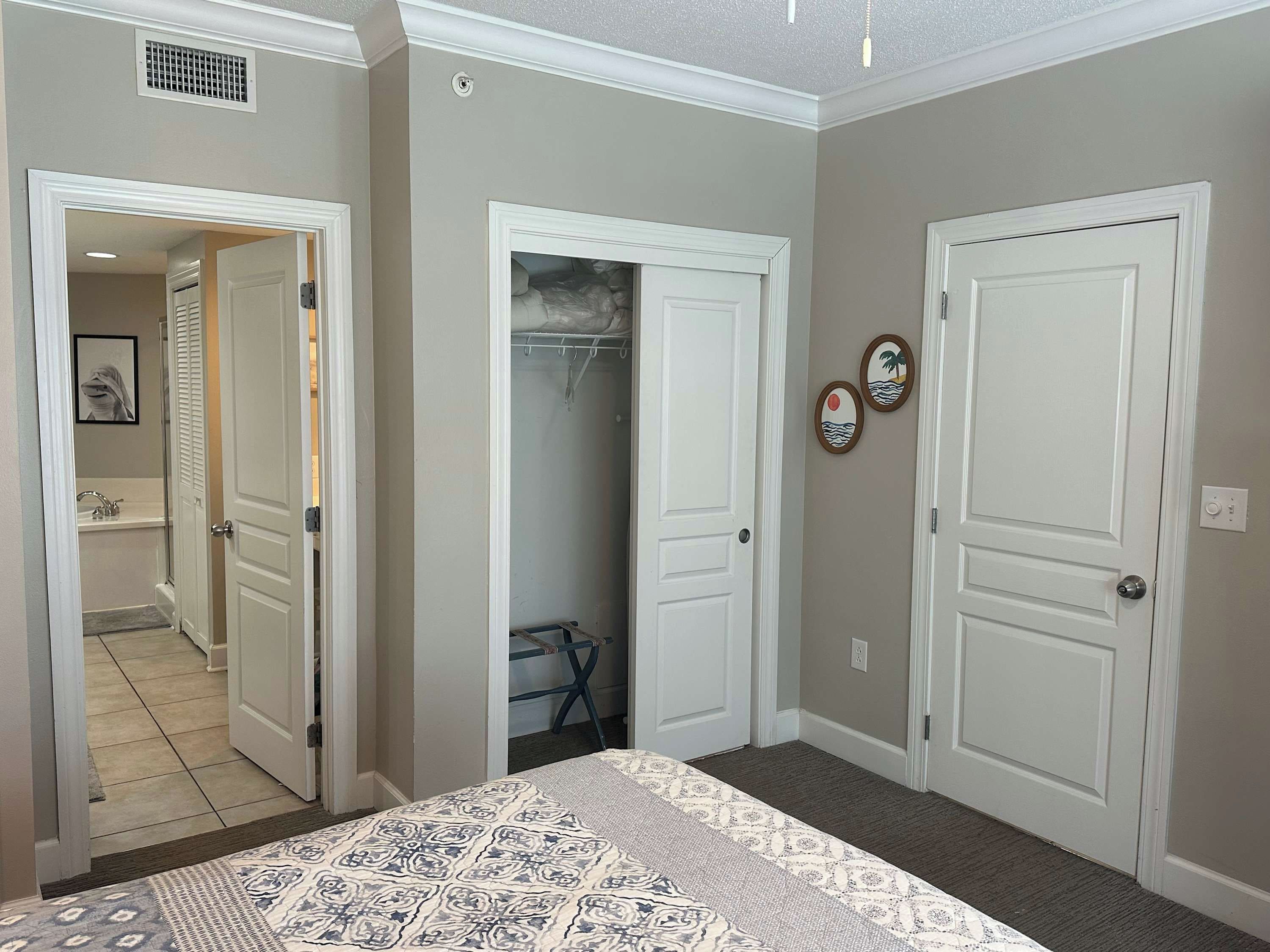 Un dormitorio con una colcha estampada, un armario con ropa colgada y una puerta con una pequeña placa decorativa.