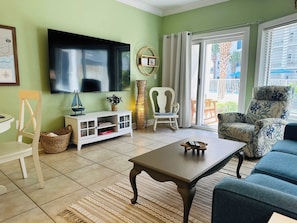 Een woonkamer met een televisie, een witte tv-meubel, een bank, een salontafel en een stoel.