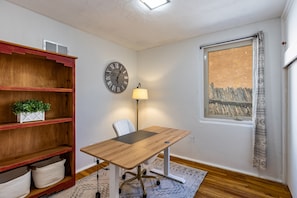 A room with a wooden desk, a chair, a clock, a lamp, a bookshelf, and a window with a view. - Casa de Vaca | Adobe Near Downtown - A/C (Santa Fe)