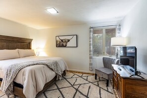 A hotel room with a bed, a desk with a lamp, a television, and a window with curtains. - Casa de Vaca | Adobe Near Downtown - A/C (Santa Fe)