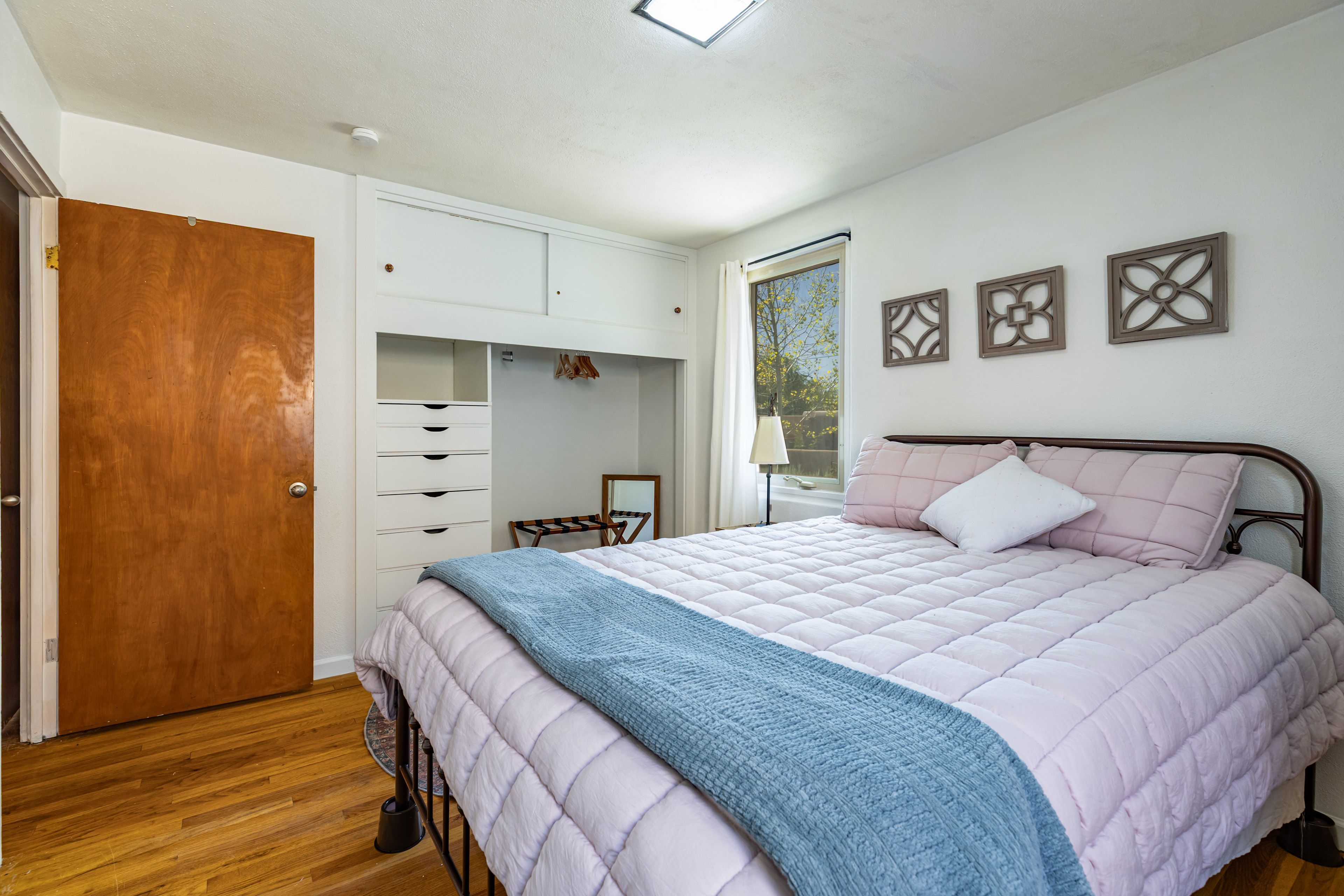 A bedroom with a bed, a wardrobe, a mirror, and a window.