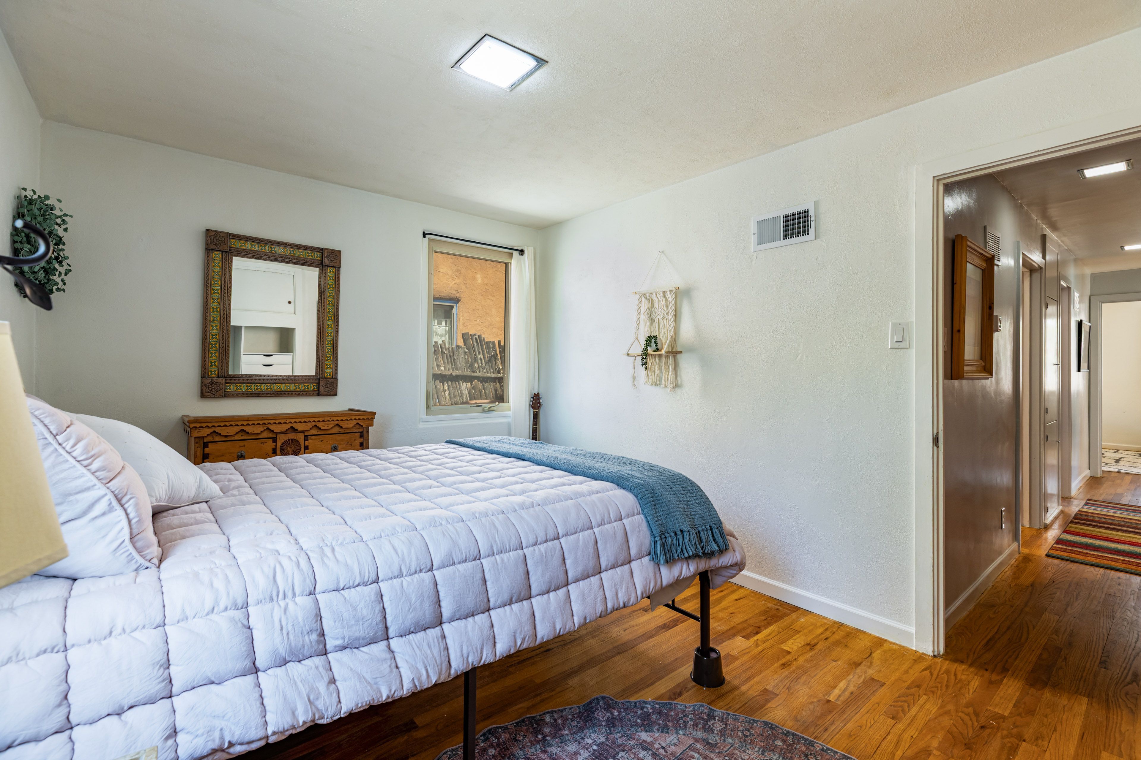 A bedroom with a bed, a dresser, a mirror, and a door leading to another room.