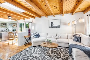 Uma sala de estar moderna com sofá branco, tapete estampado e vigas de madeira no teto.