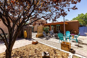 A patio with outdoor furniture, a tree, and a building with a red roof. - Casa de Vaca | Adobe Near Downtown - A/C (Santa Fe)