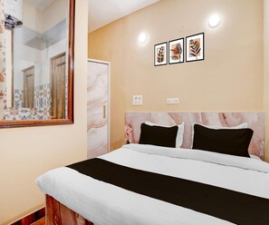 Ein Schlafzimmer mit einem Bett, einem Spiegel, einer Wand mit drei gerahmten Bildern und einer Tür.
