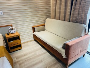 Une pièce avec un plancher en bois, un canapé, une table de chevet avec une lampe et une fenêtre avec des rideaux.